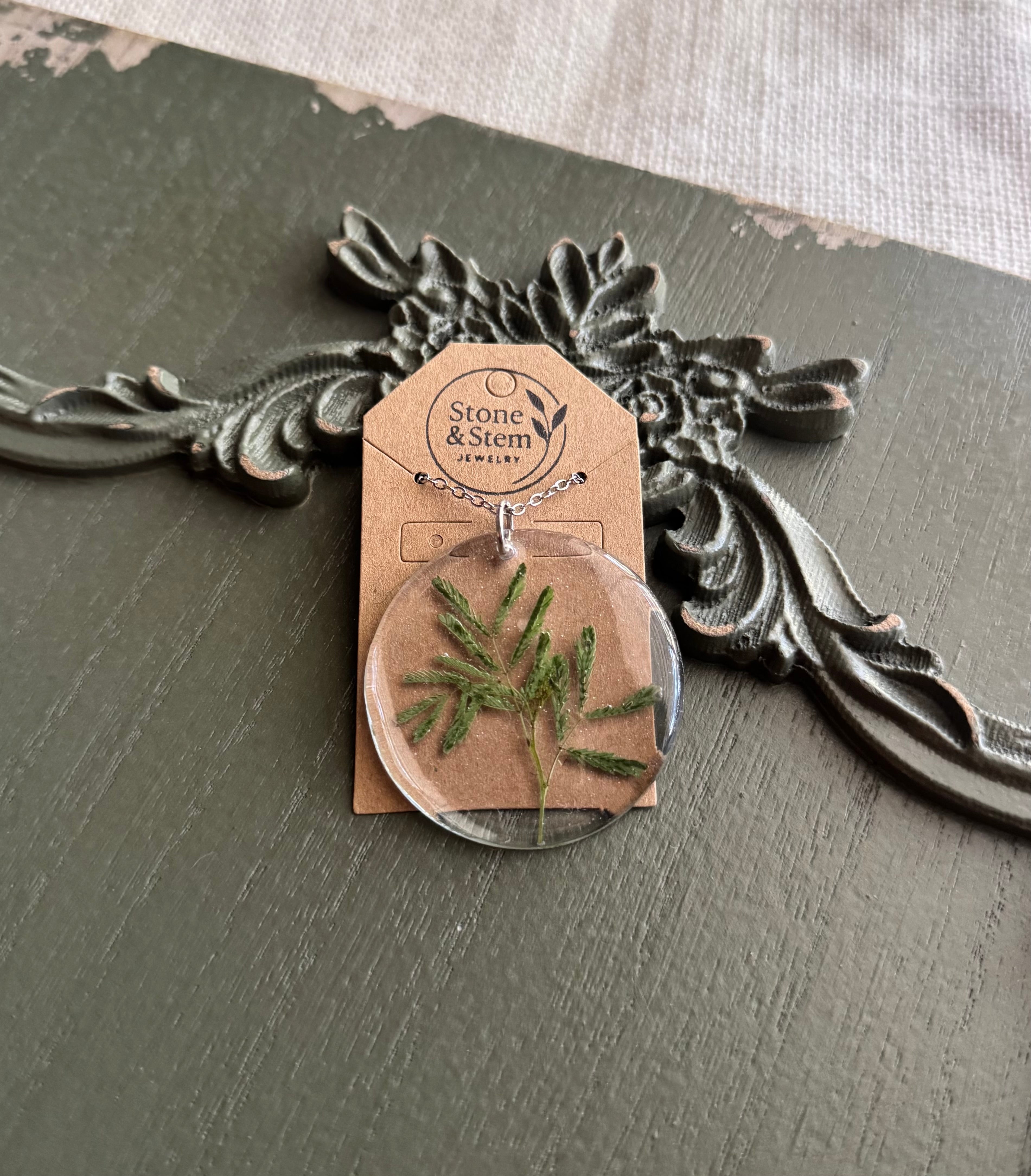 Feathery leaf preserved in clear round resin pendant necklace on silver-tone chain, displayed on Stone & Stem Jewelry card