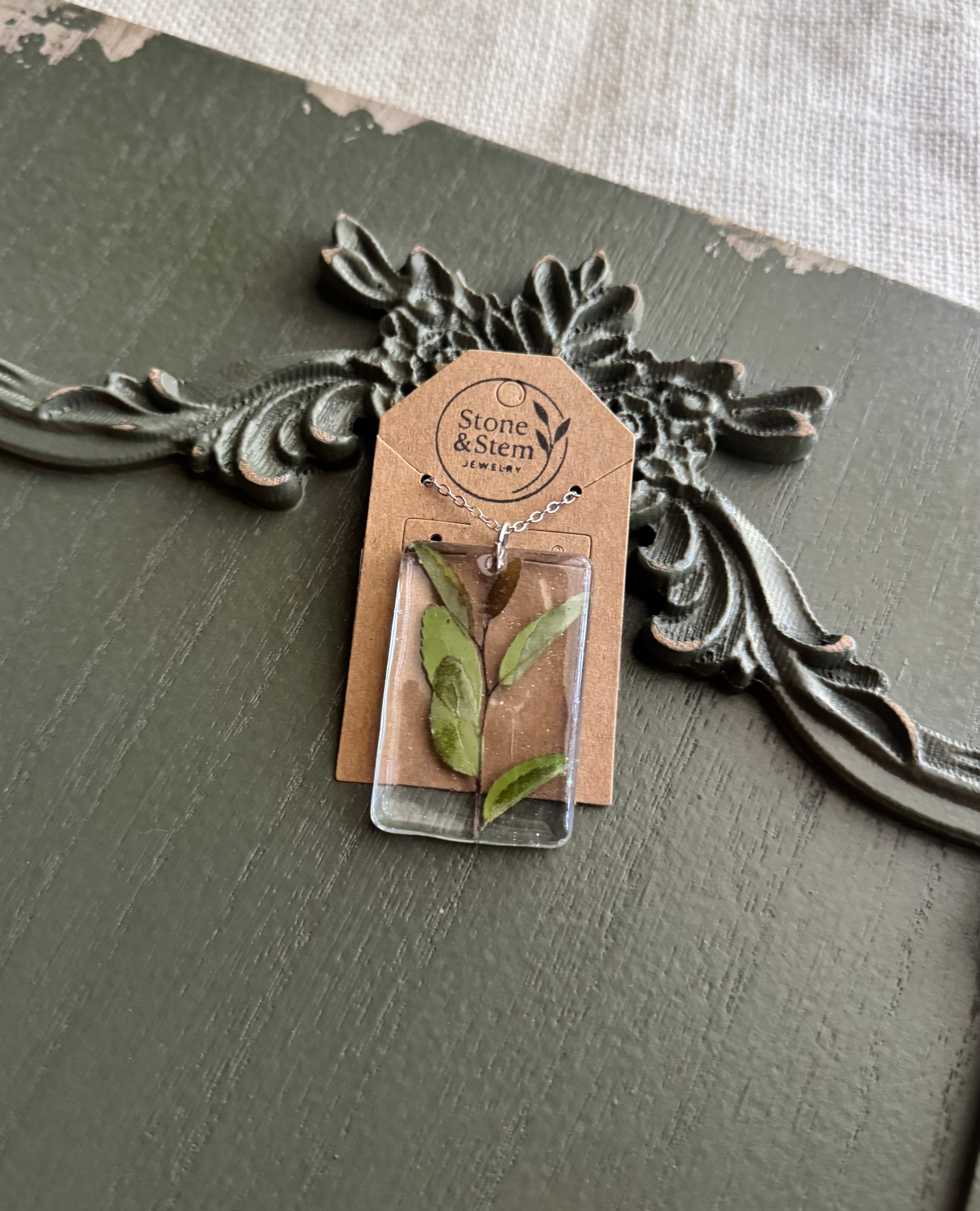 Vivid green leaf preserved in clear rectangular resin pendant necklace on silver-tone chain, displayed on Stone & Stem Jewelry card