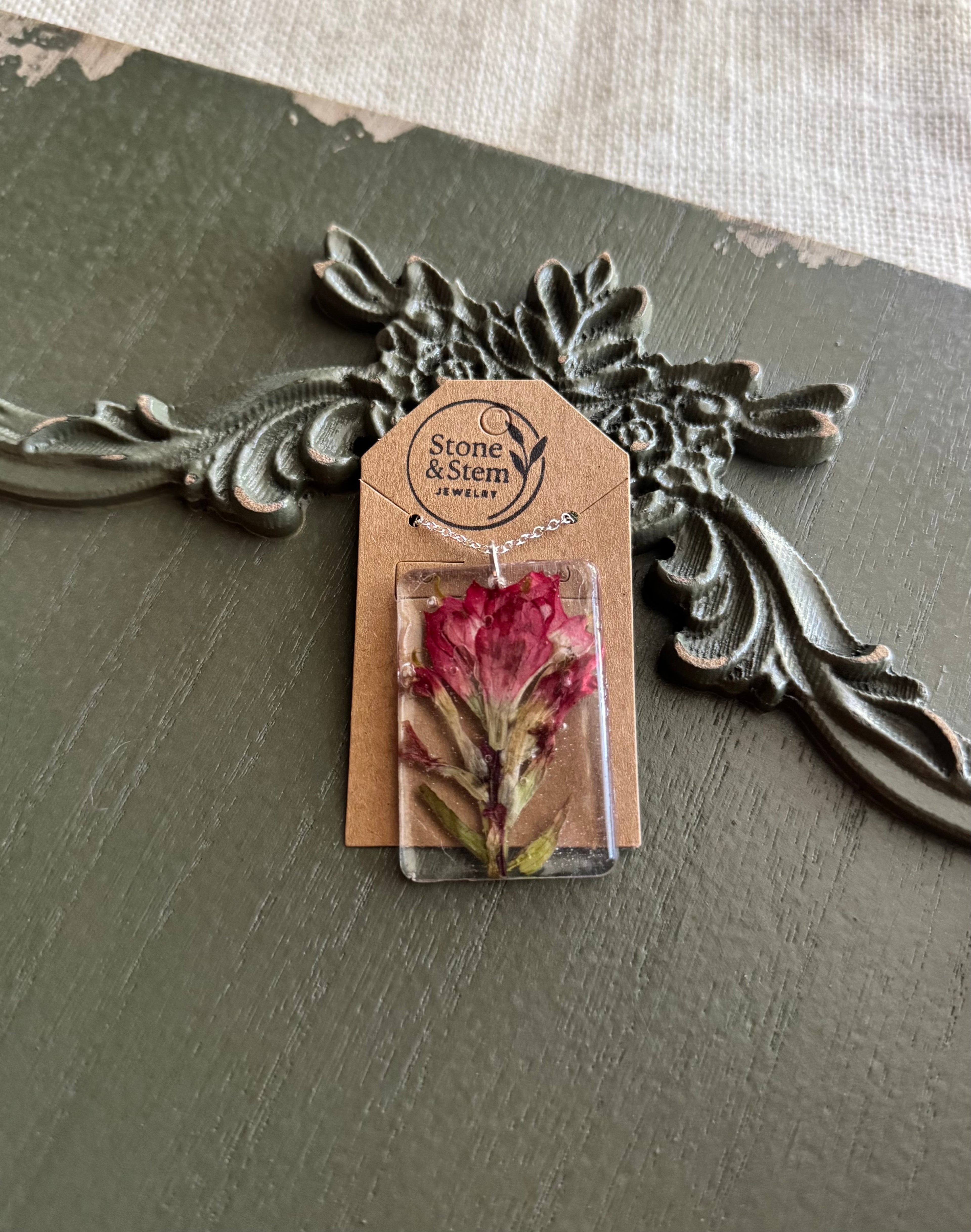 Indian Paintbrush wildflower preserved whole in clear rectangular resin pendant necklace on silver-tone chain, displayed on Stone & Stem Jewelry card