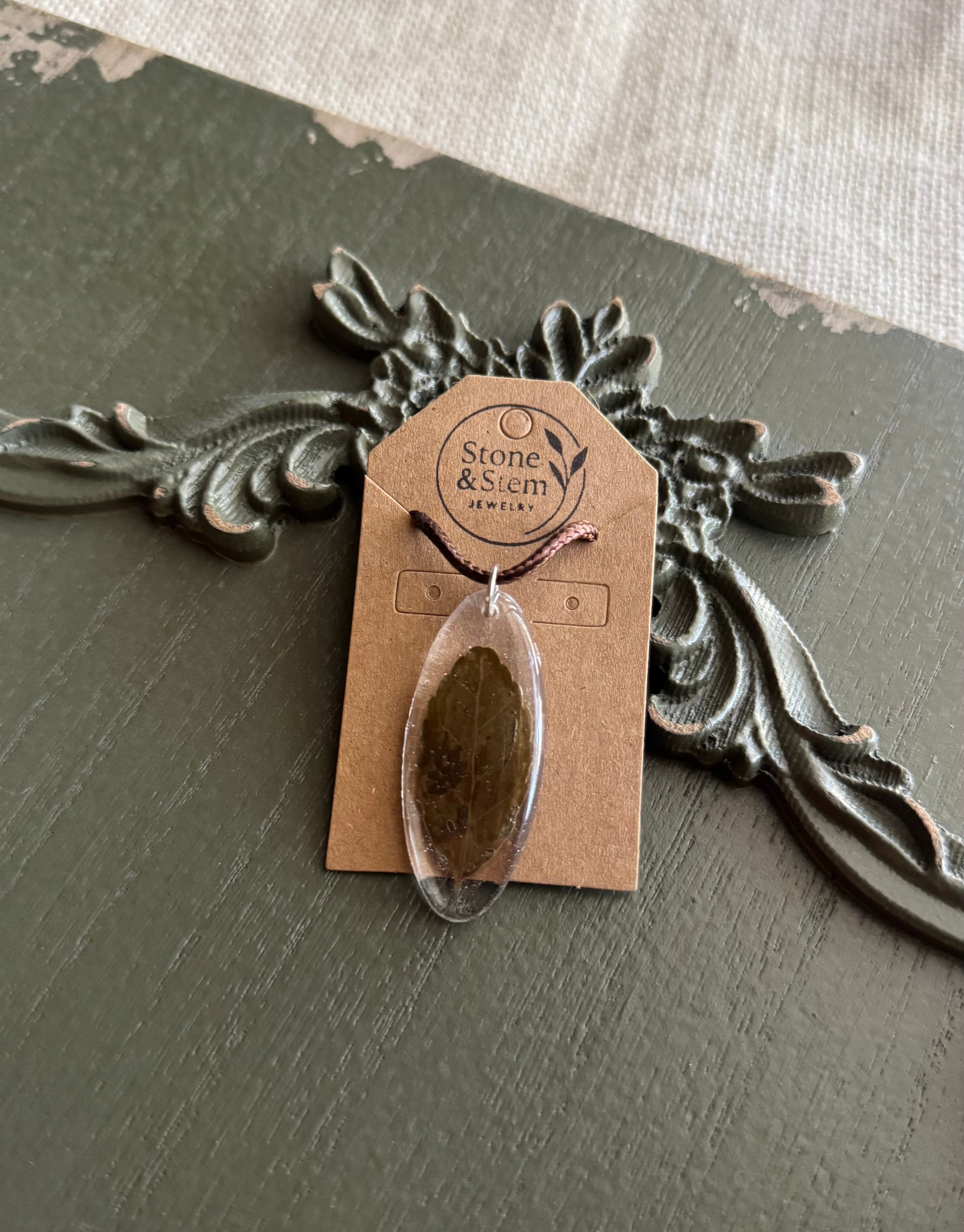 Leaf preserved in clear oval resin pendant necklace on brown waxed cord, displayed on Stone & Stem Jewelry card