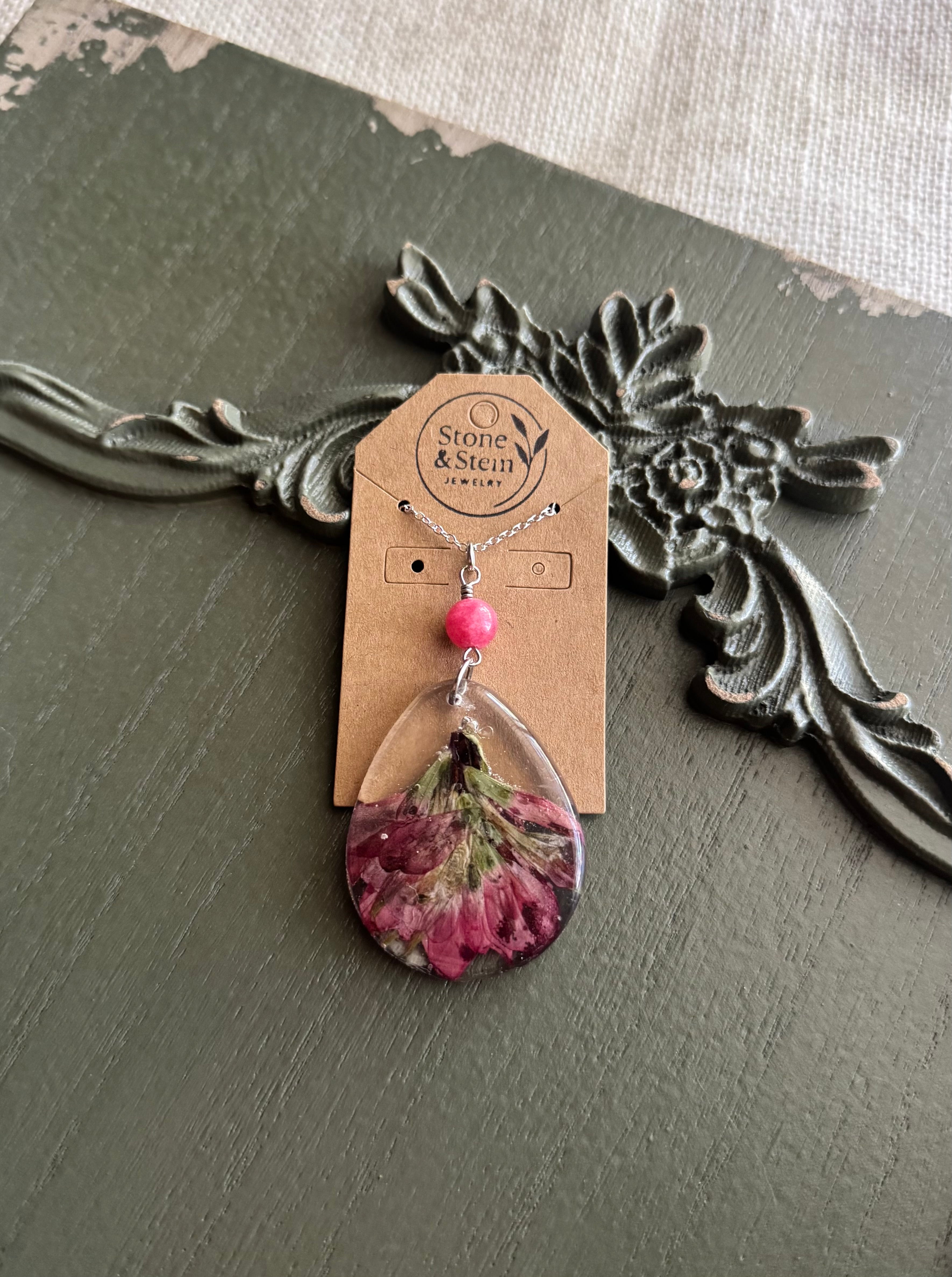 Indian Paintbrush wildflower preserved in clear teardrop resin pendant necklace with pink stone bead on silver-tone chain, displayed on Stone & Stem Jewelry card