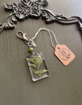Oregano sprig preserved in clear rectangular resin keychain with green stone bead and silver-tone lobster clasp, displayed on Stone & Stem Jewelry tag