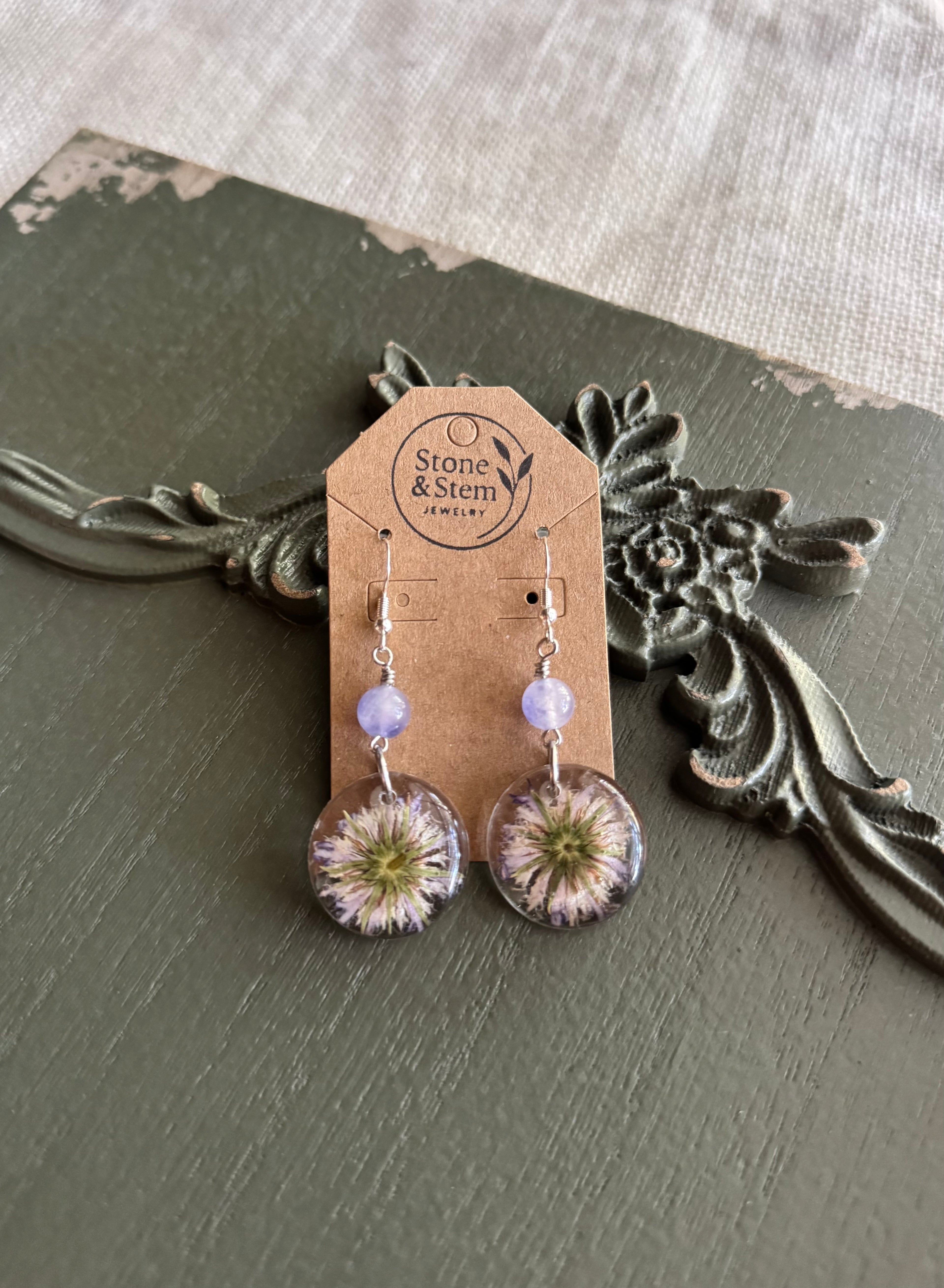 Pressed wildflower resin dangle earrings with lavender beads on a kraft paper Stone & Stem Jewelry card