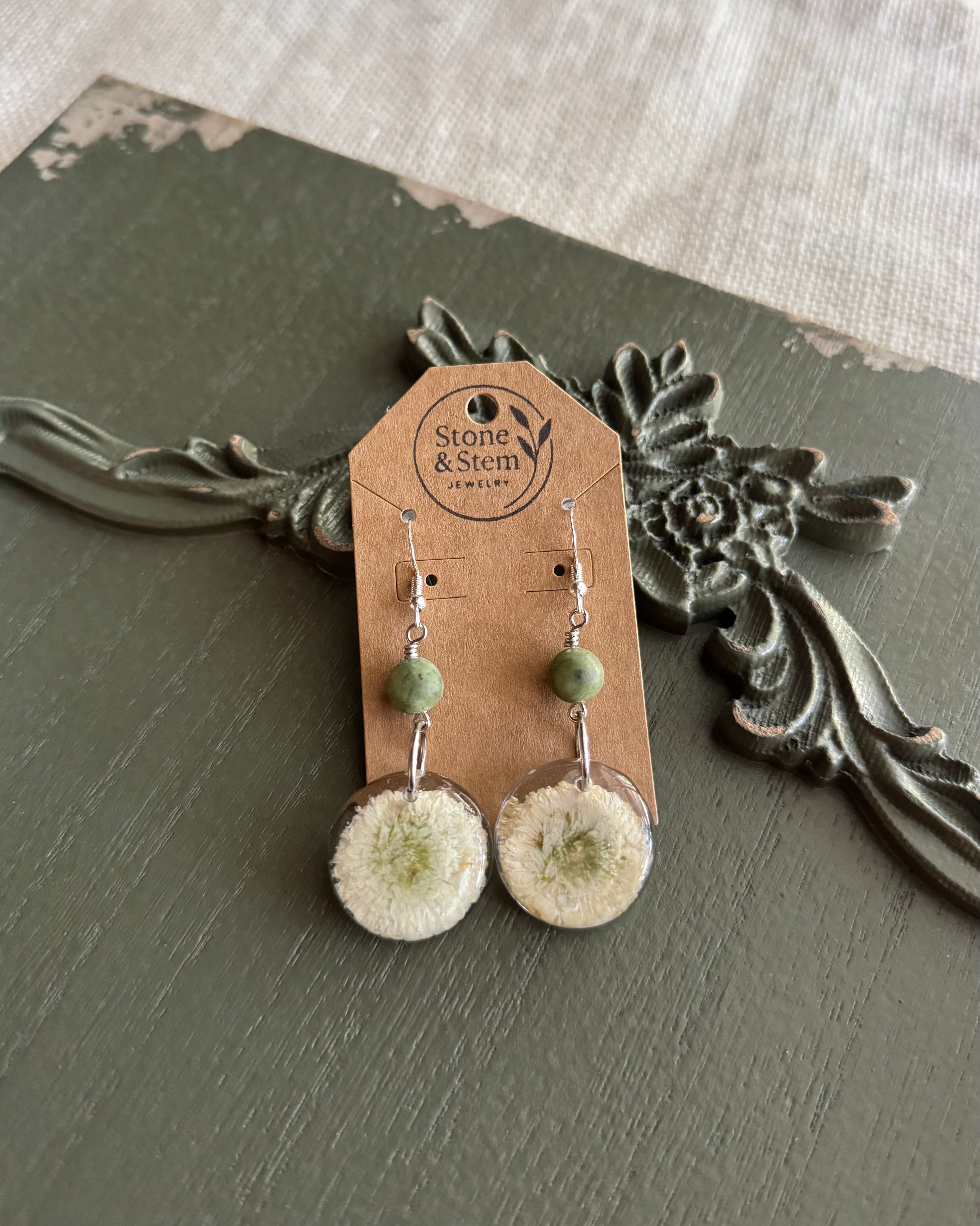 Fluffy white flower resin dangle earrings with sage green stone beads on a kraft paper Stone & Stem Jewelry card