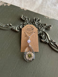 Pressed wildflower in a clear teardrop resin pendant with lavender bead on a silver chain, displayed on a Stone & Stem Jewelry kraft card