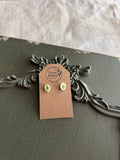 Pair of small oval white resin stud earrings with pressed green leaves on a Stone & Stem Jewelry kraft card