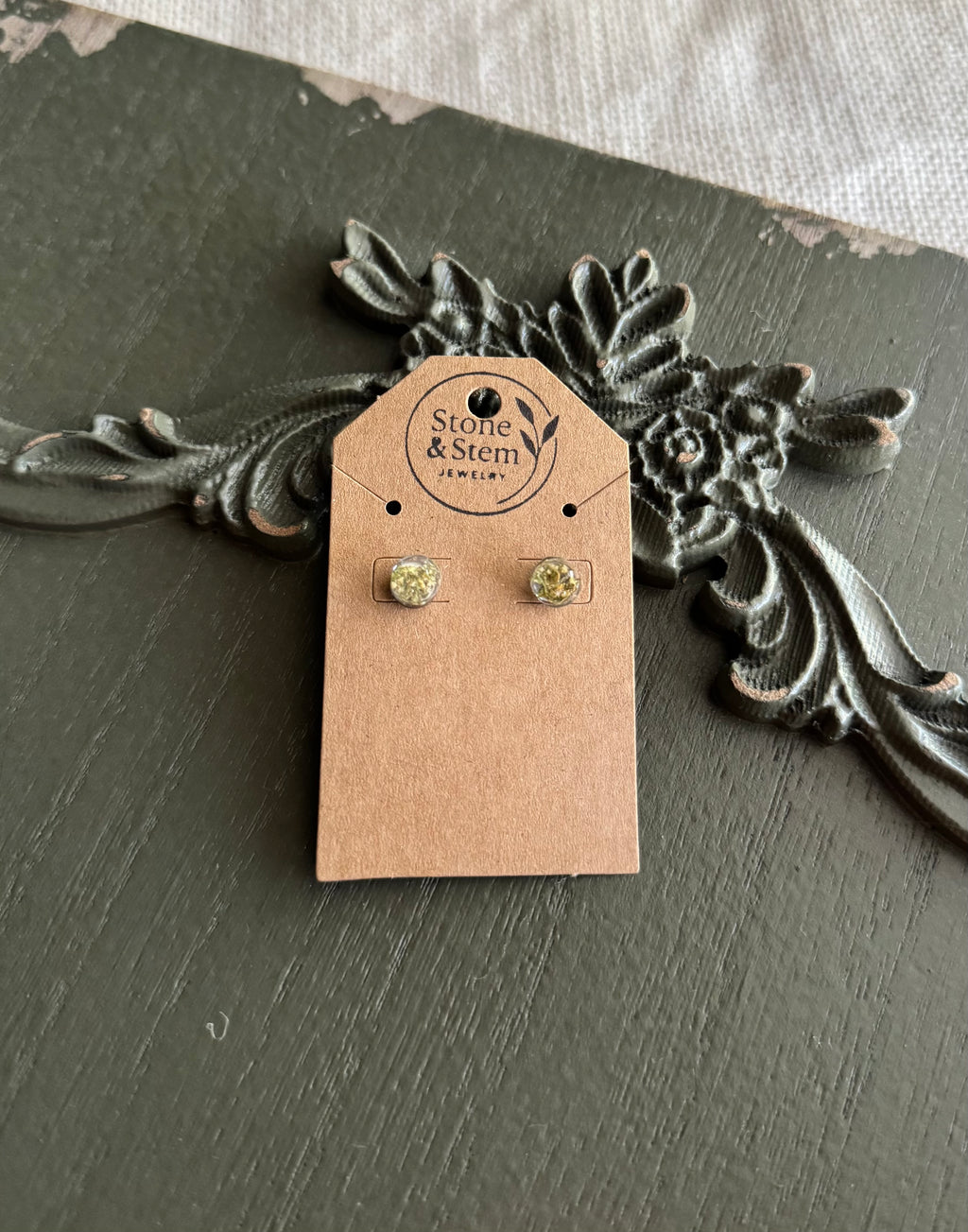 Pair of small round clear resin stud earrings with dried flowers on a Stone & Stem Jewelry kraft card