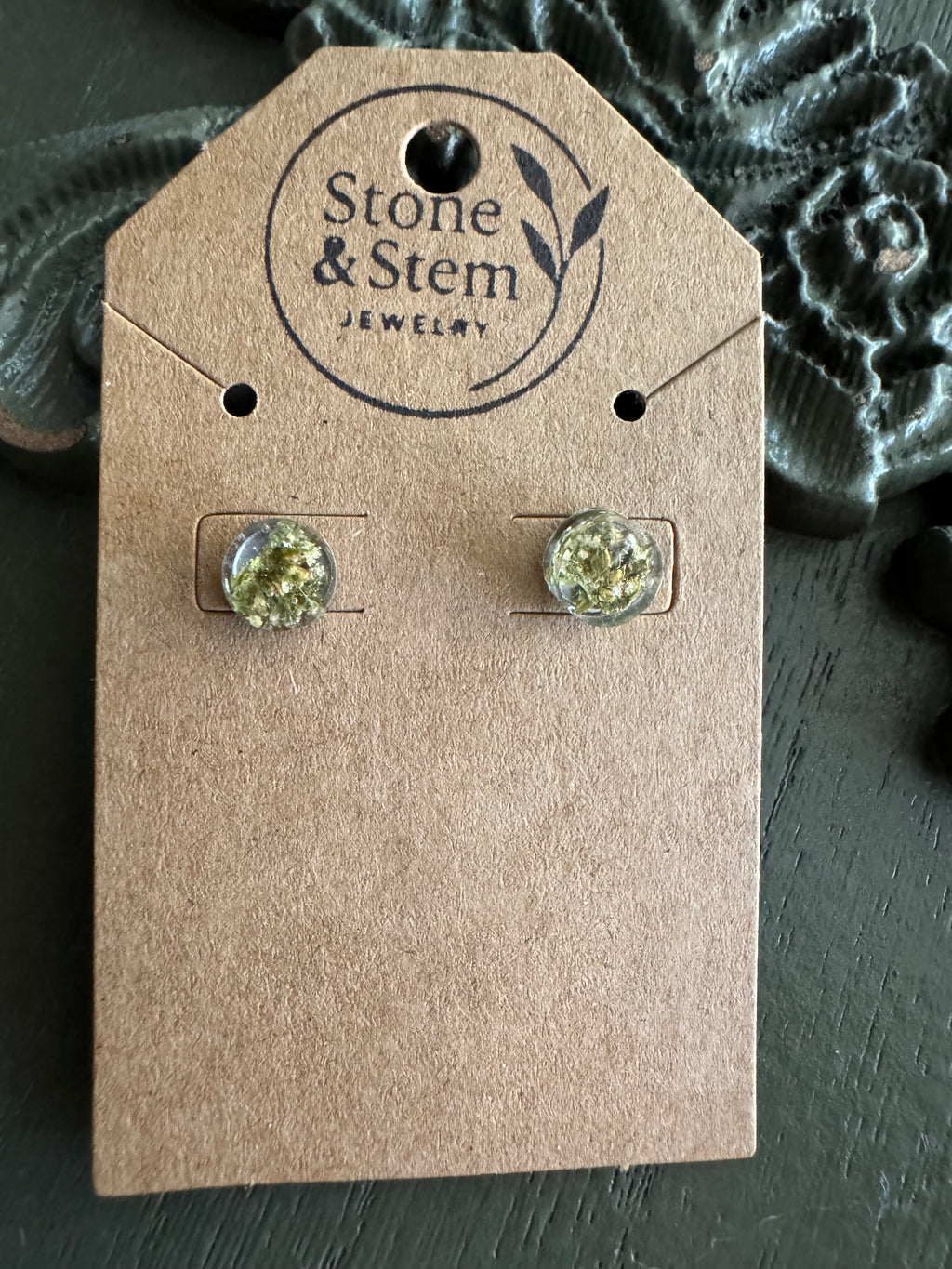 Close-up of round clear resin stud earrings showing dried flower detail on a Stone & Stem Jewelry kraft card