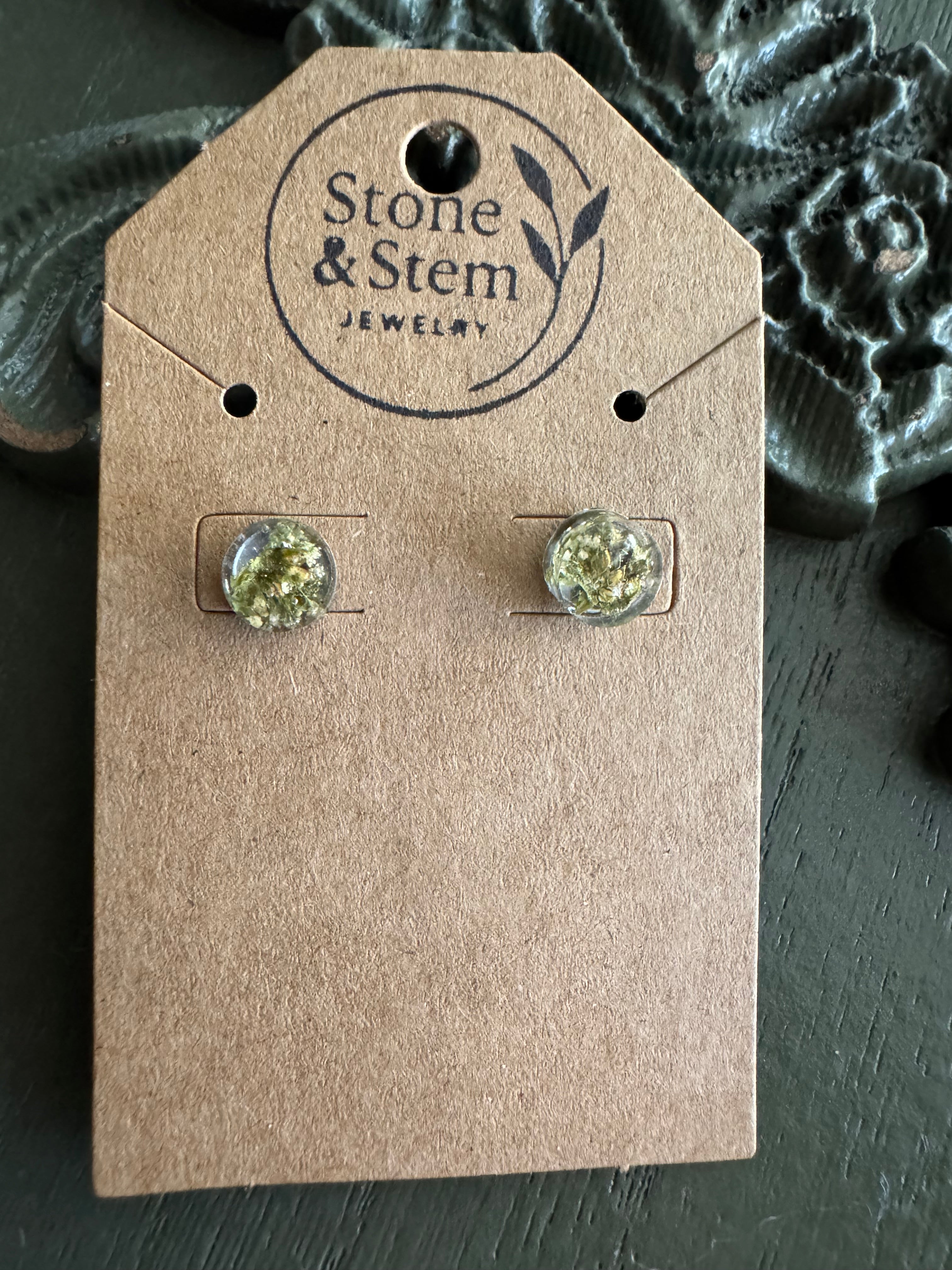 Close-up of round clear resin stud earrings showing dried flower detail on a Stone & Stem Jewelry kraft card