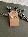 Pair of small white teardrop resin stud earrings with pressed green leaves on a Stone & Stem Jewelry kraft card