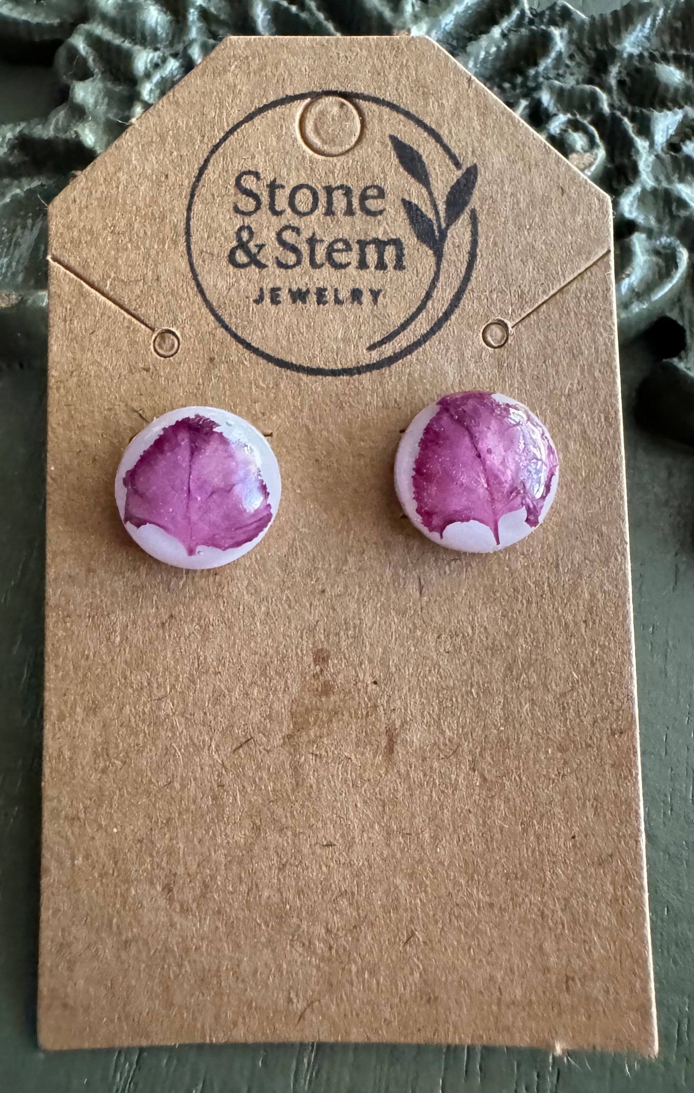 Close-up of domed white round resin stud earrings showing pressed magenta myrtle flower petal detail with natural veining on a Stone & Stem Jewelry kraft card