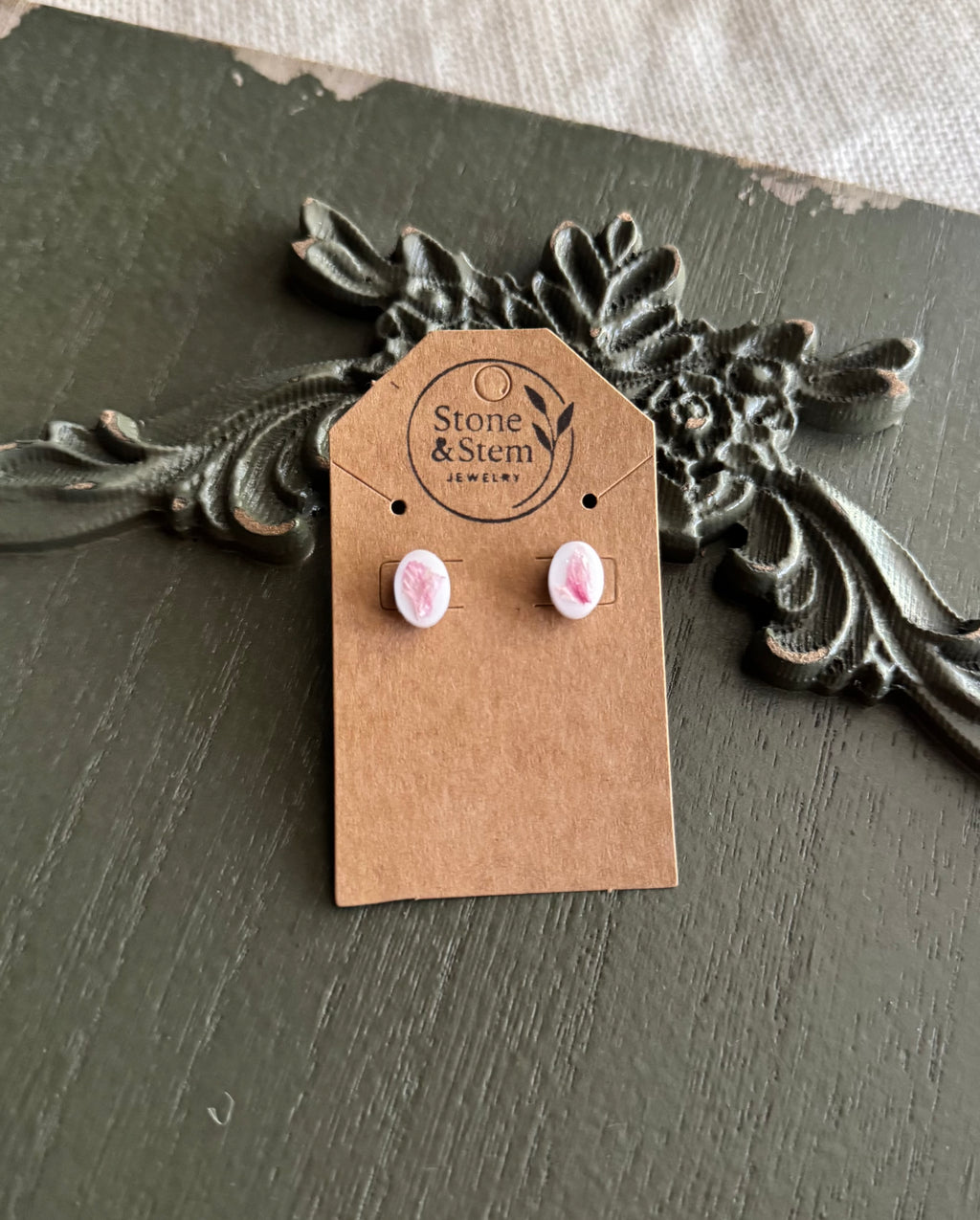 Pair of small white oval resin stud earrings with pressed pink flower petals on a Stone & Stem Jewelry kraft card