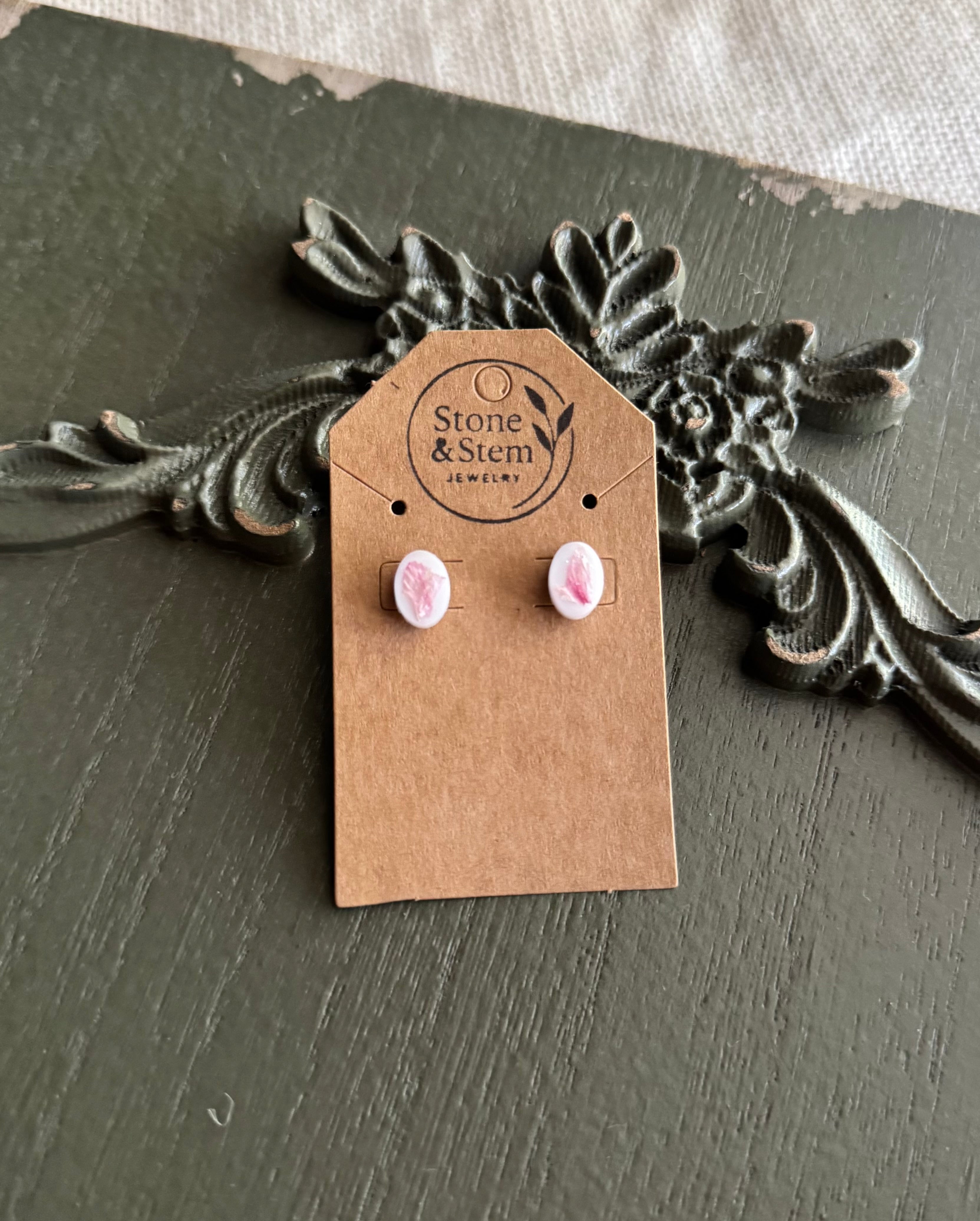 Pair of small white oval resin stud earrings with pressed pink flower petals on a Stone & Stem Jewelry kraft card