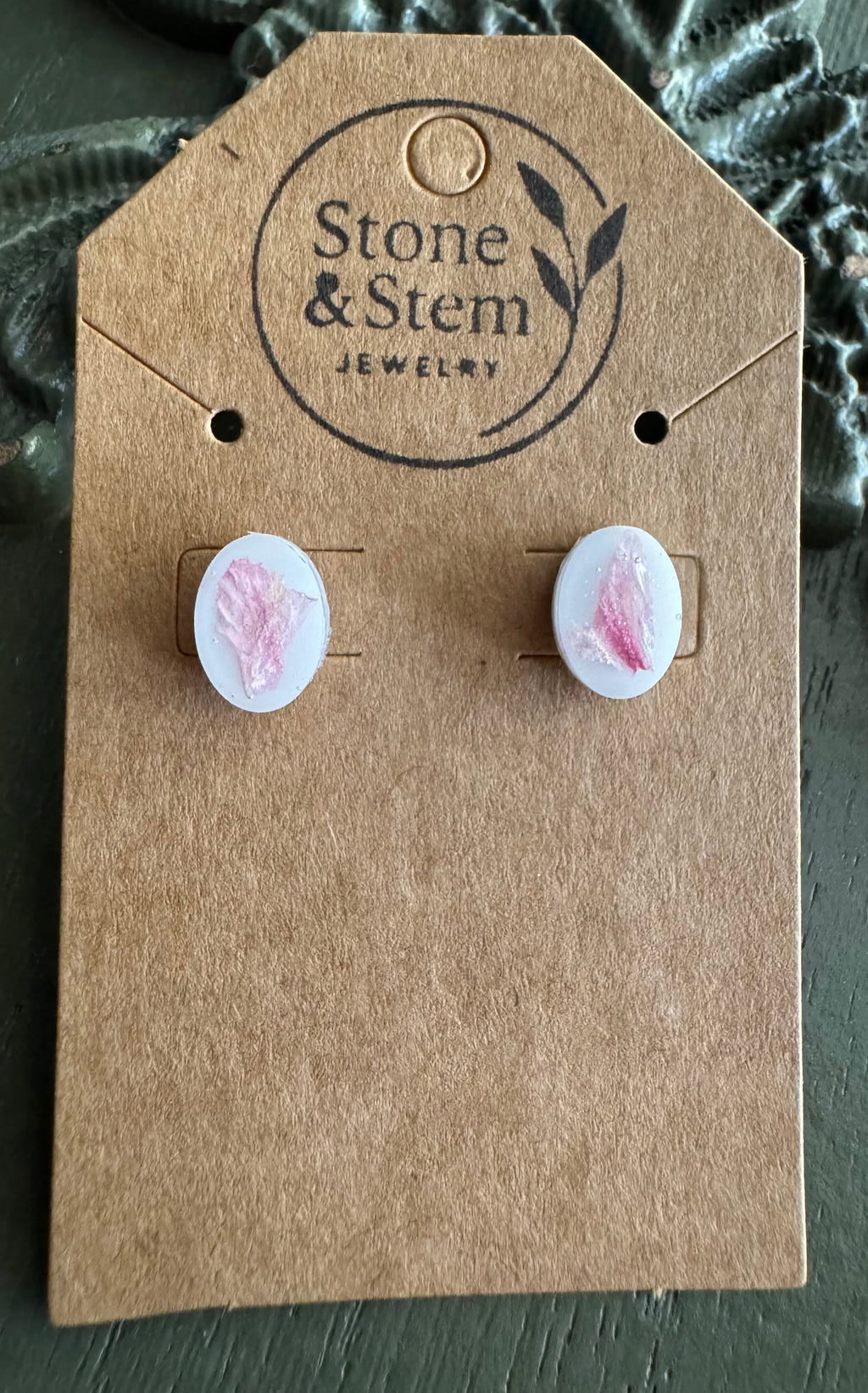 Close-up of white oval resin stud earrings showing pressed pink flower petal detail on a Stone & Stem Jewelry kraft card