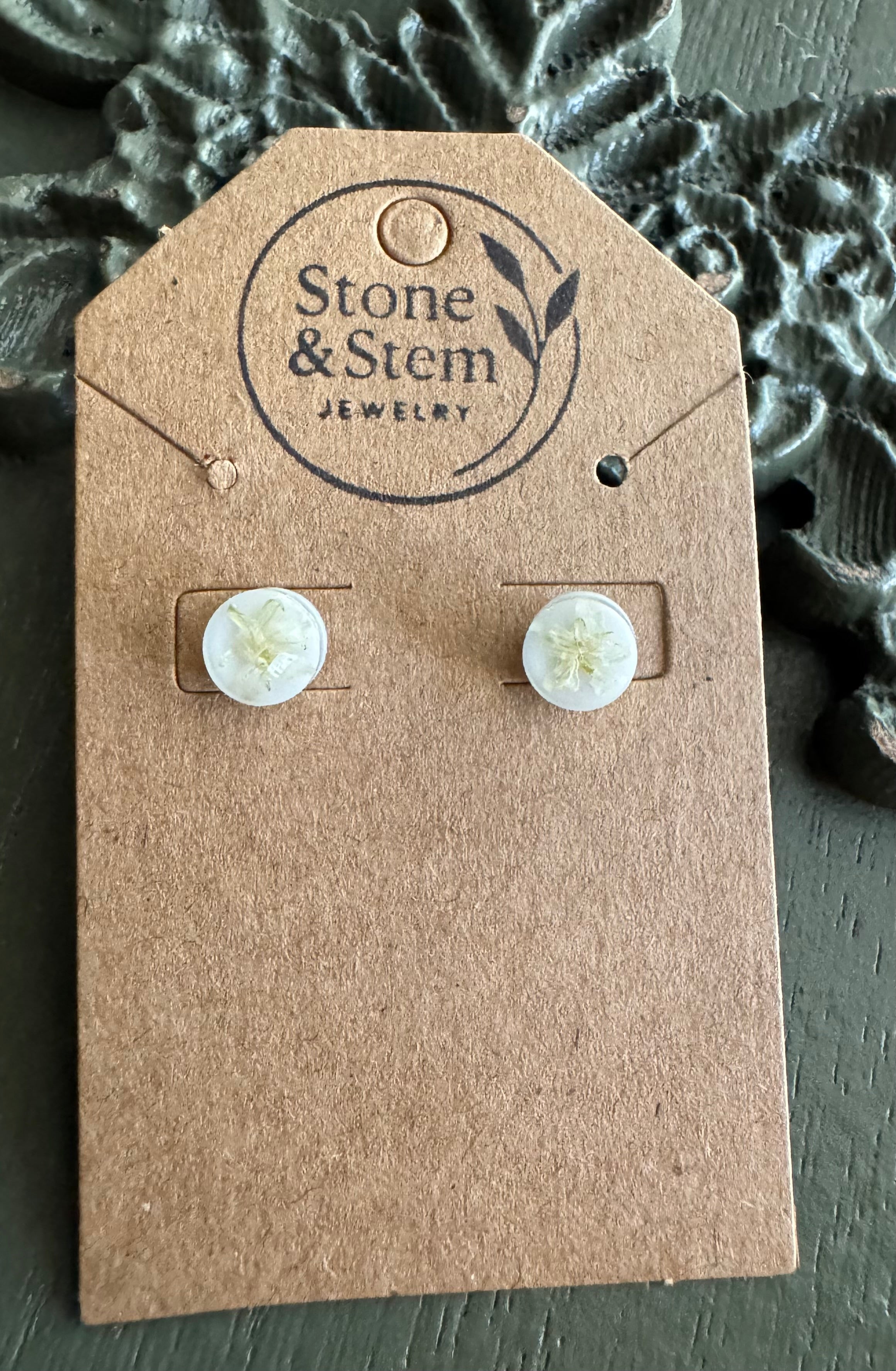 Close-up of white round resin stud earrings showing pressed white flower detail on a Stone & Stem Jewelry kraft card