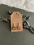 Pair of silver-framed clear round resin drop earrings with pressed purple and yellow wildflowers on 925 sterling silver ear wires on a Stone & Stem Jewelry kraft card
