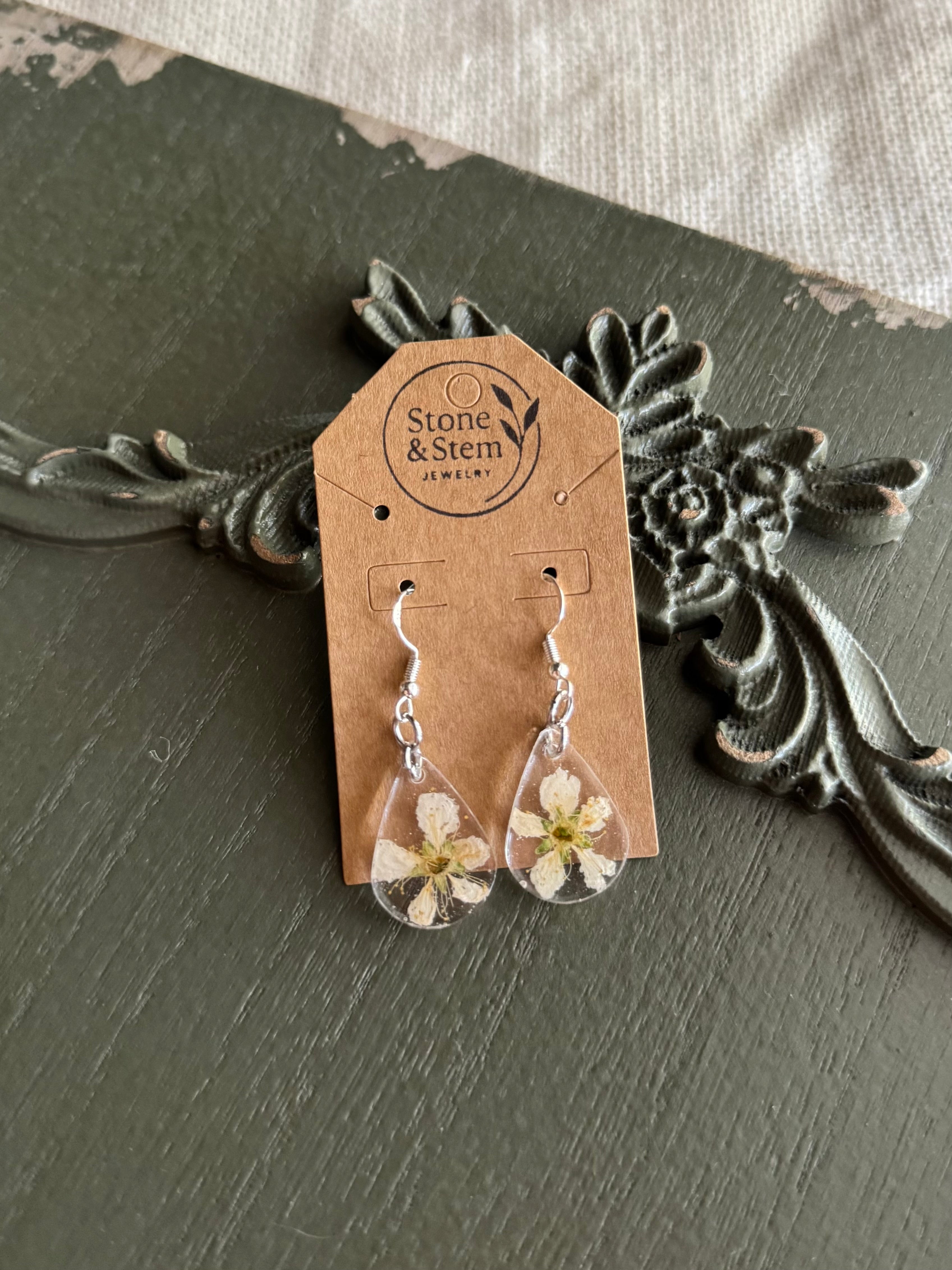 Pair of clear teardrop resin drop earrings with a real pressed white fruit tree blossom on 925 sterling silver ear wires on a Stone & Stem Jewelry kraft card