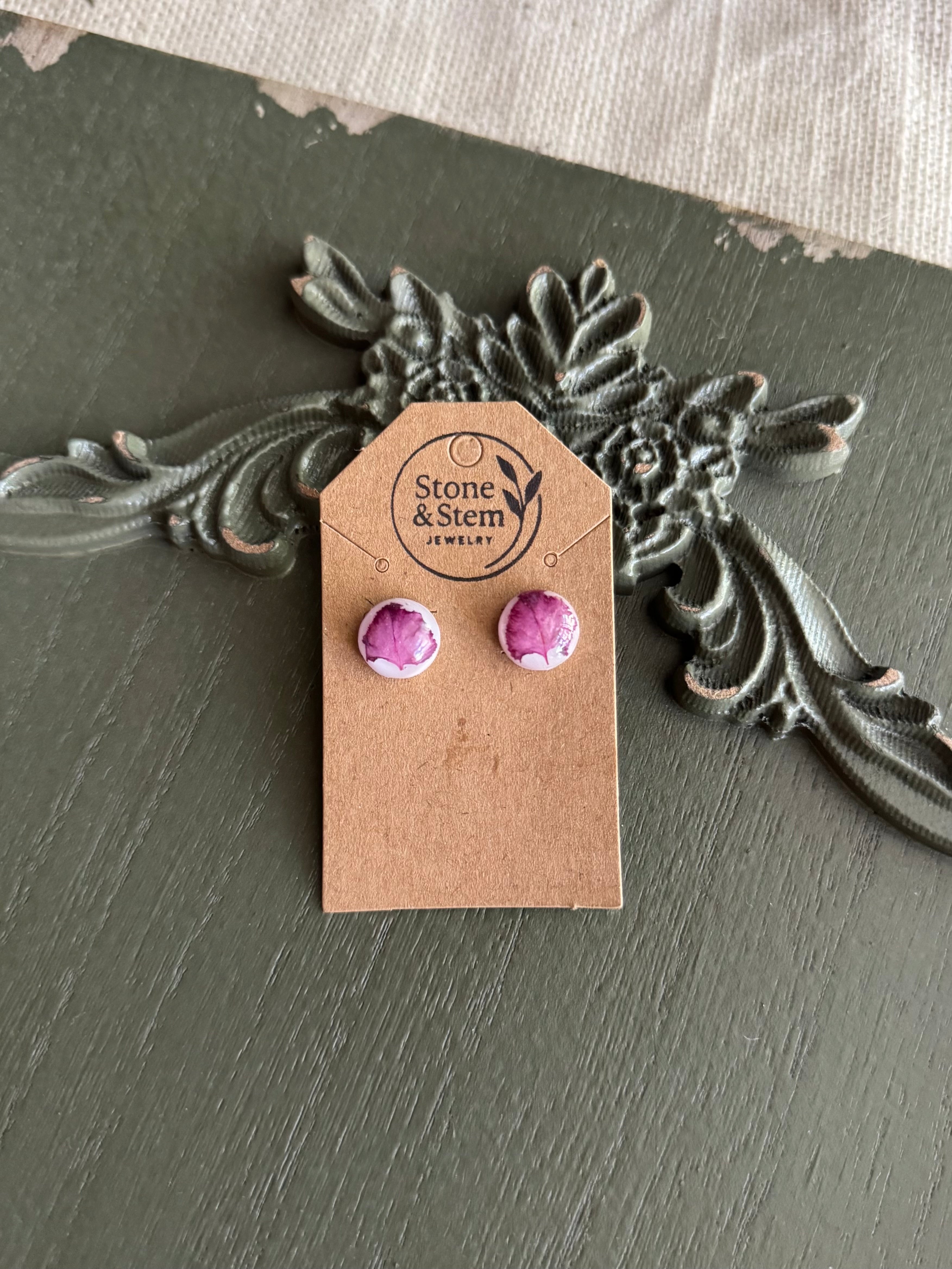 Pair of small domed white round resin stud earrings with pressed magenta myrtle flower petals on a Stone & Stem Jewelry kraft card